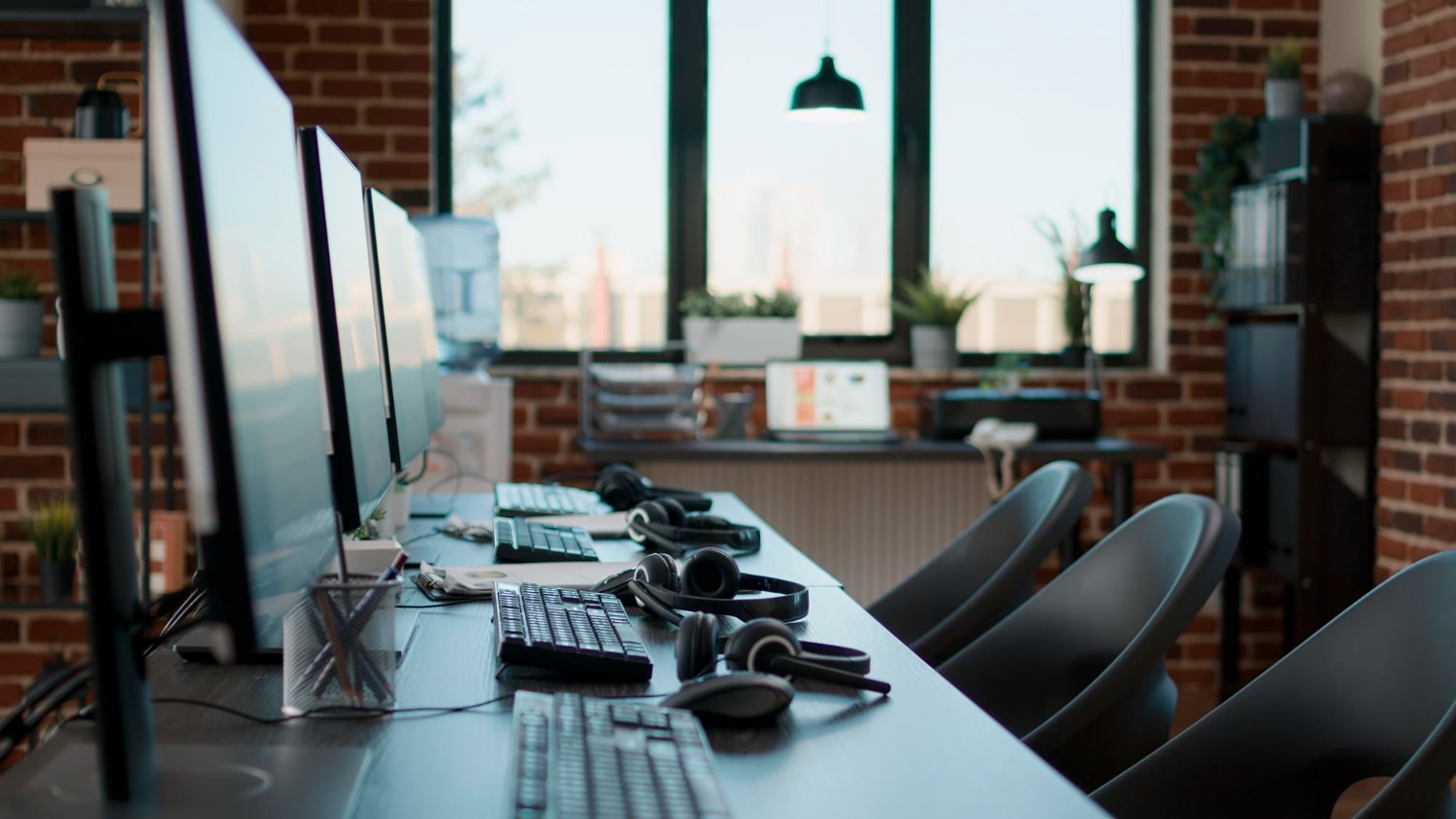 A row of computer stations with headsets and keyboards in an industrial-style office, ready for employees. This empty but prepared workspace represents Workforce Agility, emphasizing the importance of Staffing Solutions for Business Growth that ensure businesses can quickly scale operations when needed.